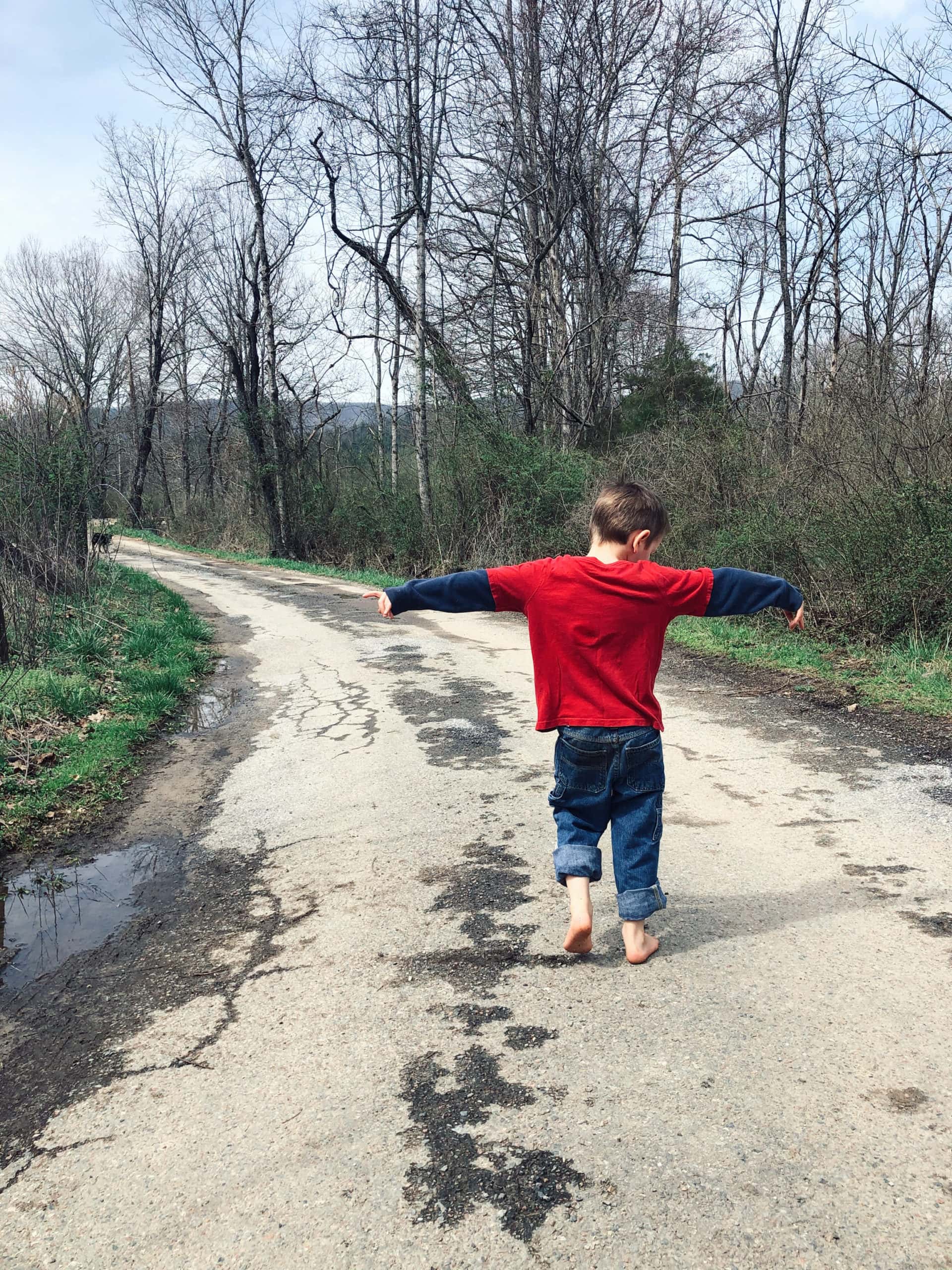 little boy walking down road with arms outstretched