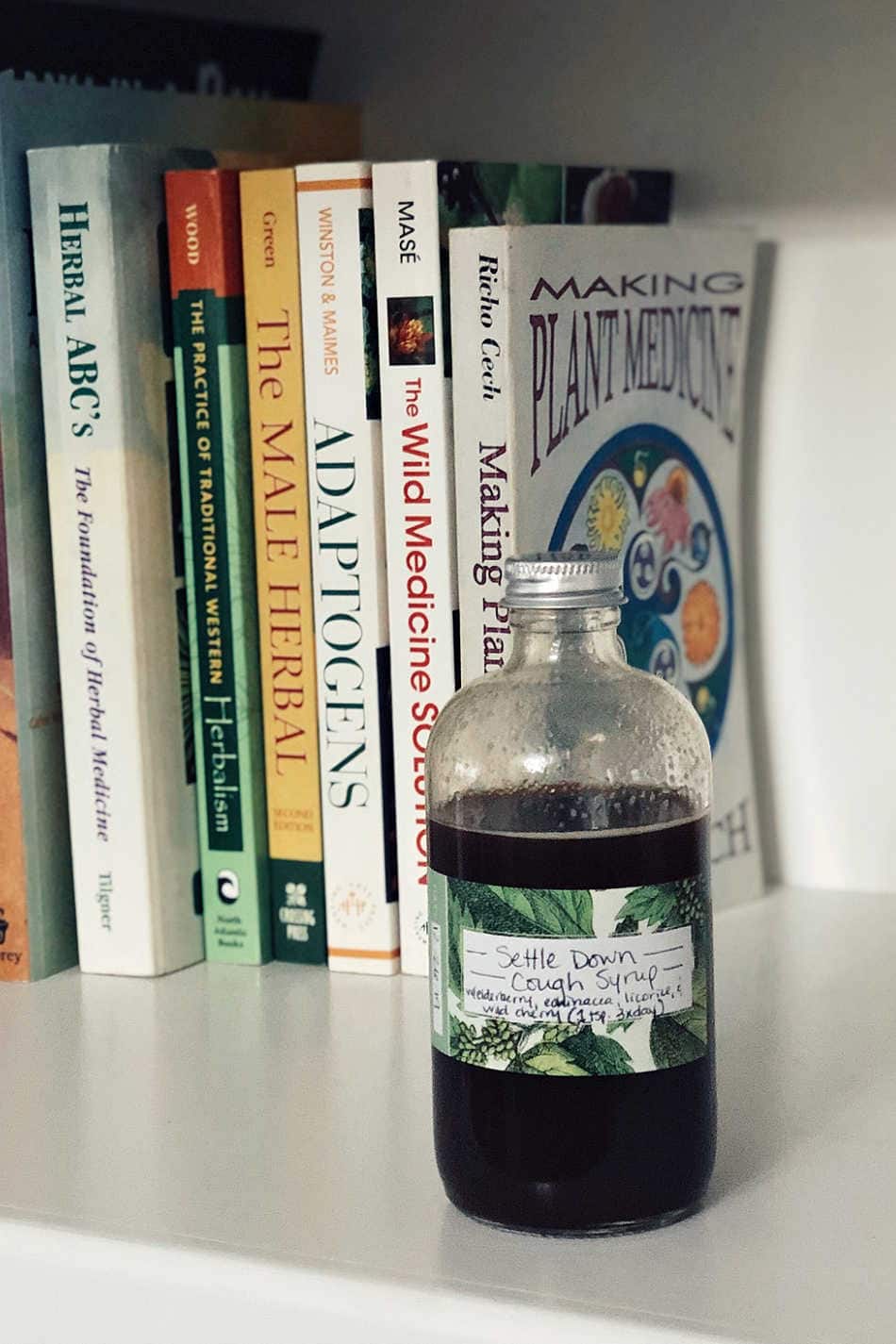 herbal syrup on shelf next to herb books